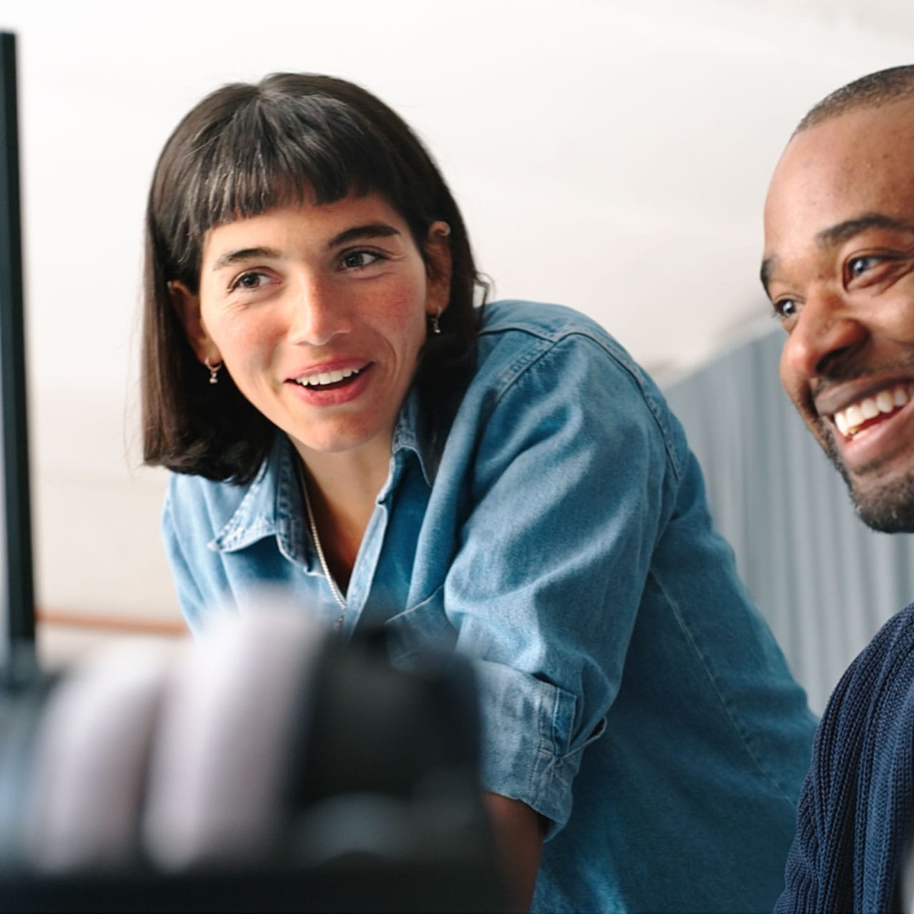A smiling woman in denim shirt and a man are looking at a screen.